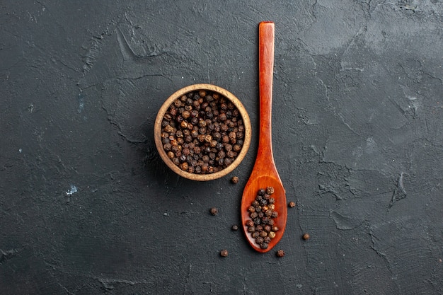 top view black pepper bowl wooden spoon on dark surface copy place