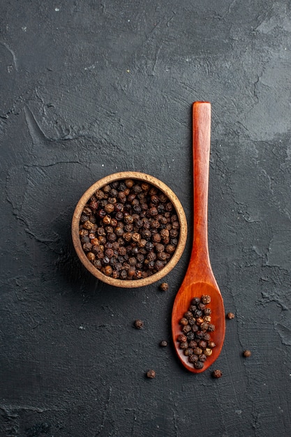 Free photo top view black pepper bowl wooden spoon on dark surface copy space