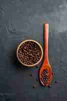 Foto gratuita vista dall'alto ciotola di pepe nero cucchiaio di legno su superficie scura copia spazio