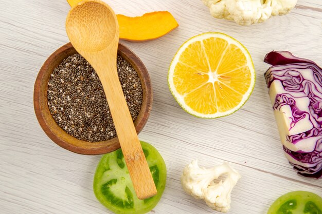 Top view black pepper powder in small bowl wooden spoon cut vegetables on white wooden table