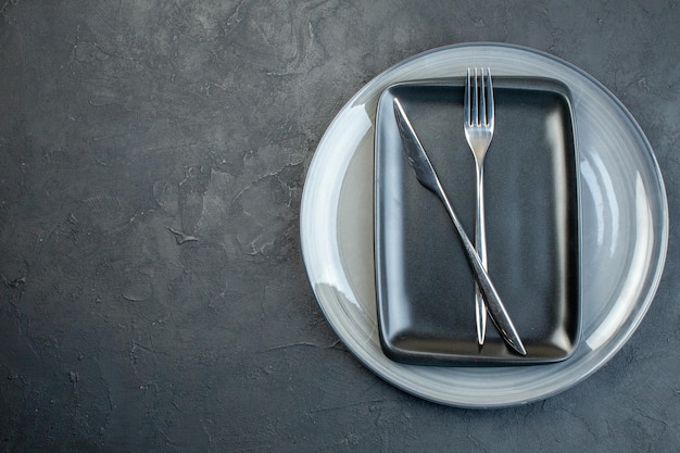 Top view black plate with fork knife and gray plate on dark background silverware diner colourful femininity hunger grace cutlery