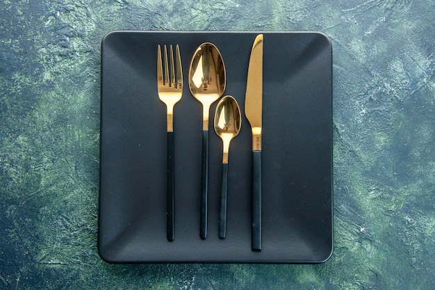 Бесплатное фото Вид сверху черные тарелки с золотыми ложками нож и вилка на темном фоне цвет еда ужин кухня ресторан столовые приборы