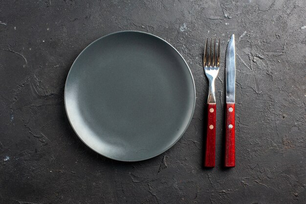 Top view black round plate a fork and knife on black surface