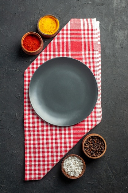 Top view black round platter on red and white checkered napkin bowls with turmeric red pepper powder sea salt black pepper on dark table