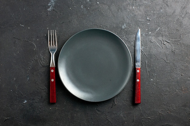 Вид сверху вилка и нож для черной салатной тарелки на черной поверхности