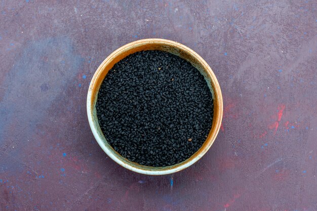 Top view black seasonings inside round pot on grey background.