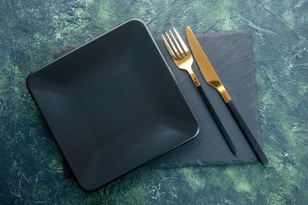 вид сверху черная квадратная тарелка с золотой вилкой и ножом на темном фоне цветная еда ресторан столовые приборы ужин кухня