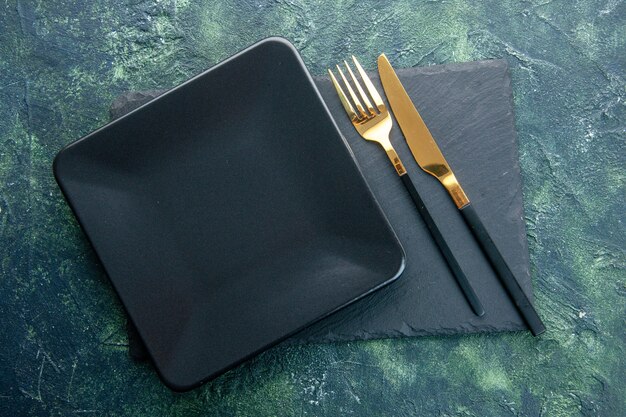 暗い背景色の食品レストランカトラリーディナーキッチンに金色のフォークとナイフで上面図黒い正方形のプレート