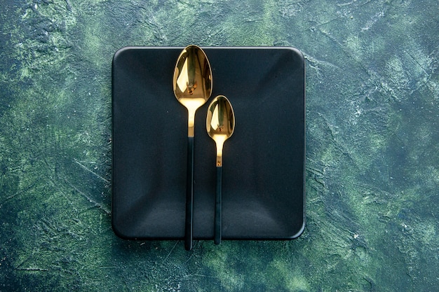 Free photo top view black square plate with golden spoons on dark blue background dinner restaurant food cutlery color meal utencil