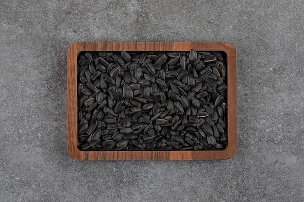 Top view of black sunflower seeds on wooden plate over grey surface