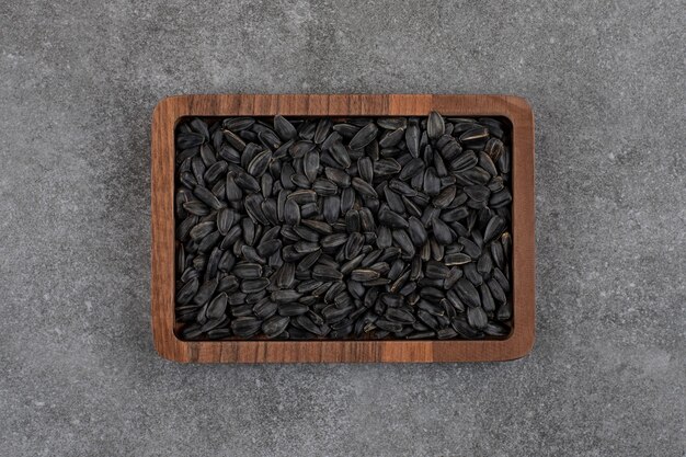 Top view of black sunflower seeds on wooden plate over grey surface