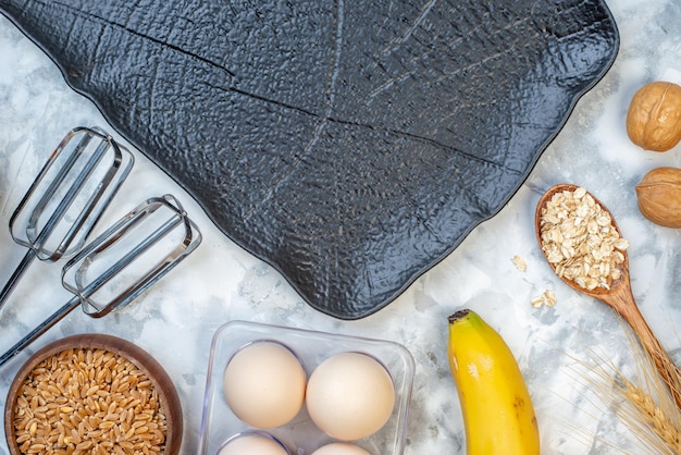 Top view of black tray and fresh bananas oats spoon brown rice in a pot eggs on ice background