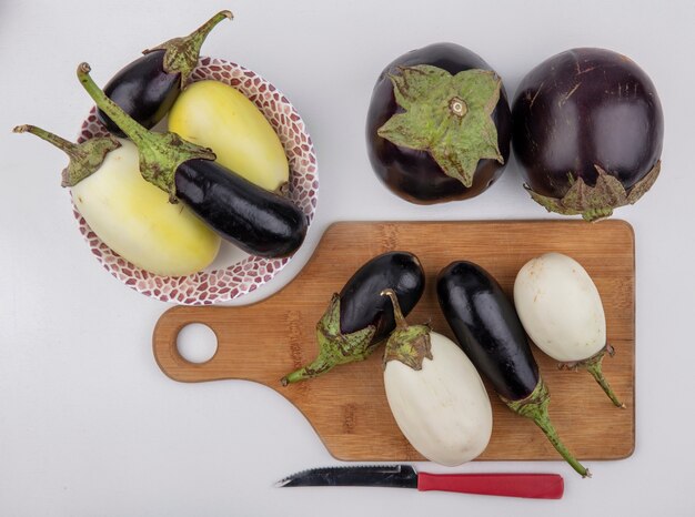 Top view black and white eggplant on a cutting board with a knife and in a plate  on a white background