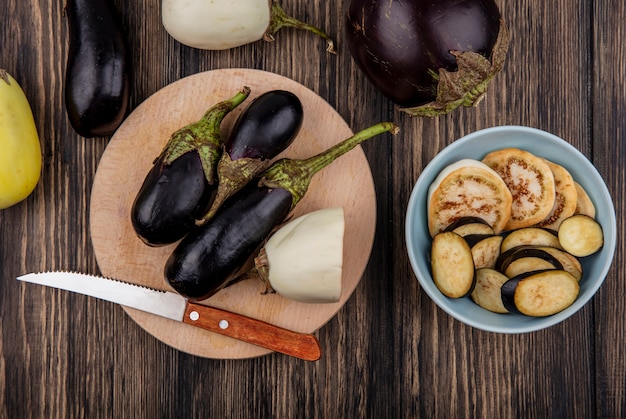 Top view black and white eggplant on cutting board with knife and slices in plate on wooden background