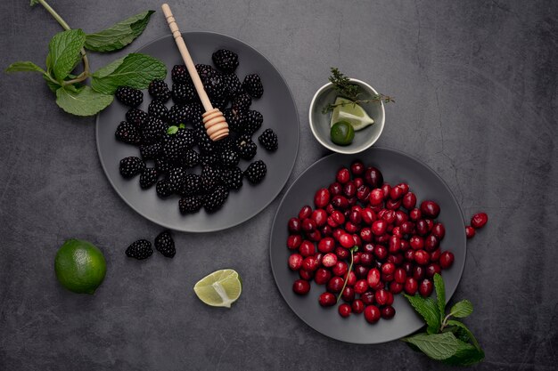 Top view of blackberries and cranberries on plate with mint and honey dipper