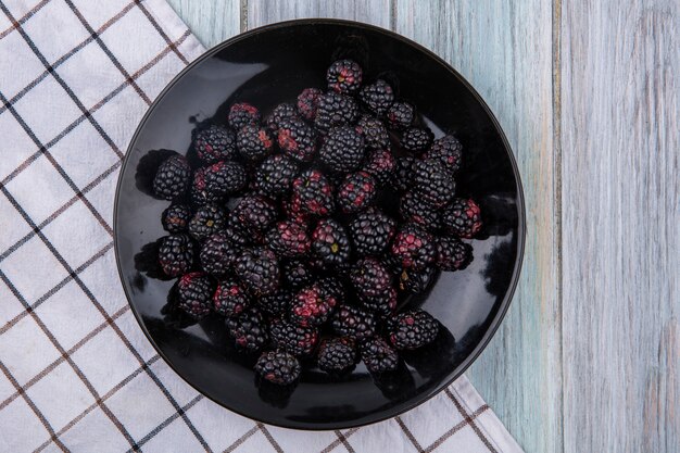 Top view of blackberry on a black plate with a checkered towel on a gray surface