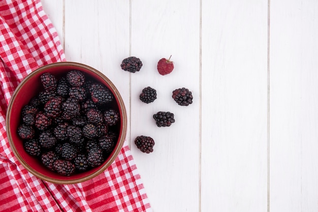 Free photo top view of blackberry in a bowl on a red checkered towel on a white surface