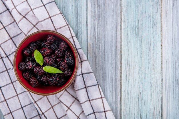 Top view of blackberry in a bowl on a white checkered towel on a gray surface