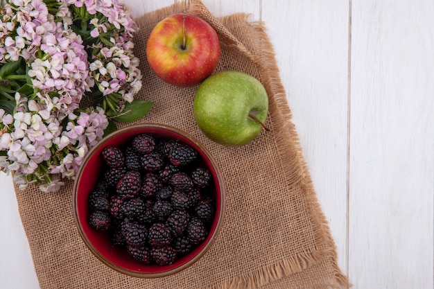 Top view of blackberry in a bowl with apples on a beige napkin with flowers