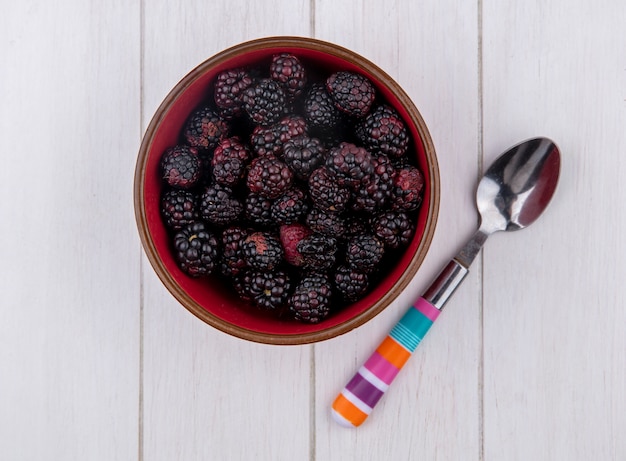 Top view of blackberry in a bowl with a teaspoon on a white surface