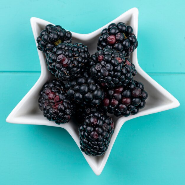 Top view of blackberry in a saucer in the form of a star on a light blue surface