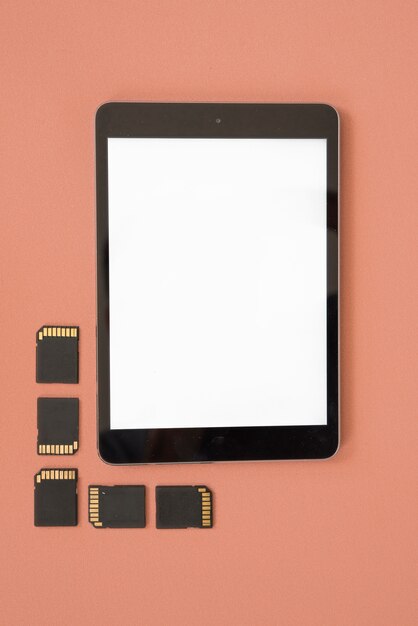 Top view of blank digital tablet with memory cards over orange background