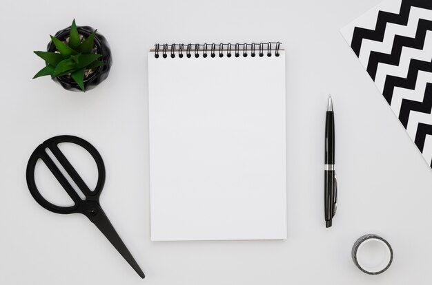 Top view of blank notebook with scissors and plant