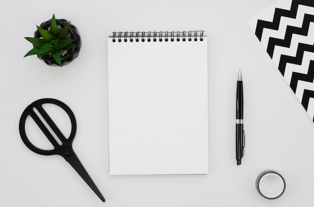 Top view of blank notebook with scissors and plant