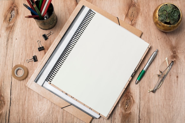 Top view of blank spiral book; eye glasses; plant and office supplies on table