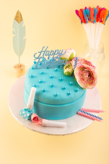 黄色の机のお祝いパーティーの誕生日ケーキの上に花と上から見る青い誕生日ケーキ