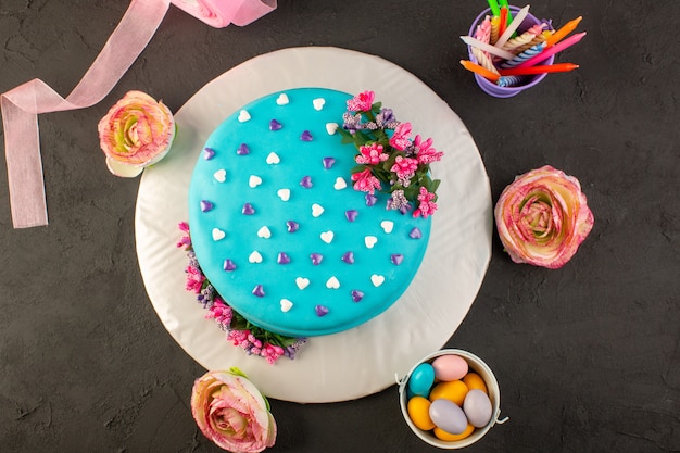 A top view blue birthday cake with flowers and candies all around