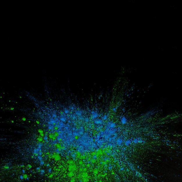 Top view of blue and green holi color powder over black background