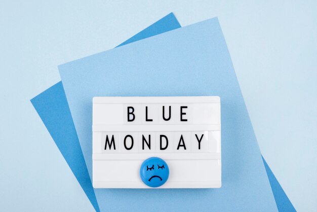 Top view of blue monday light box with sad face and paper