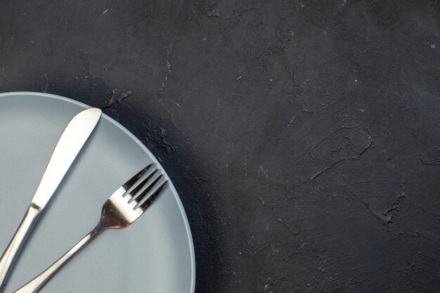 Top view blue plate with fork and knife on dark surface