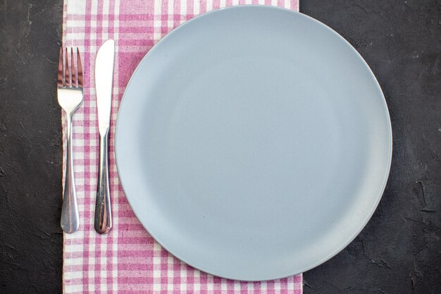 Вид сверху синяя тарелка с вилкой и ножом на темной поверхности