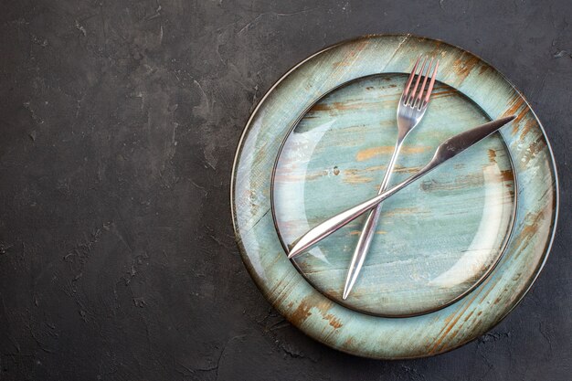 Top view blue plate with fork and knife inside on dark surface