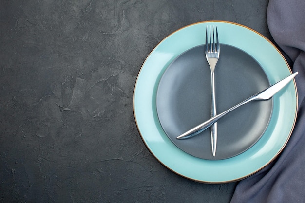 Вид сверху синяя тарелка с серой тарелкой, вилкой и ножом на темном фоне столовое серебро, красочная женственность, голодные дамы, благодать, закусочная