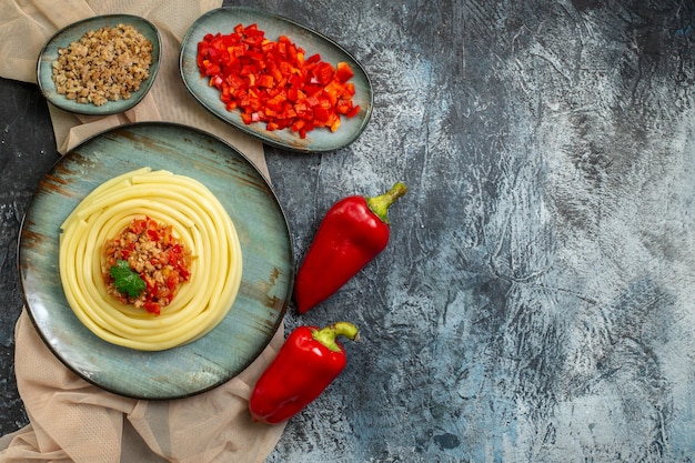 Вид сверху на синюю тарелку с вкусной пастой, подаваемой с помидорами и мясом на нарезанном полотенце коричневого цвета, целым перцем и спиральной записной книжкой