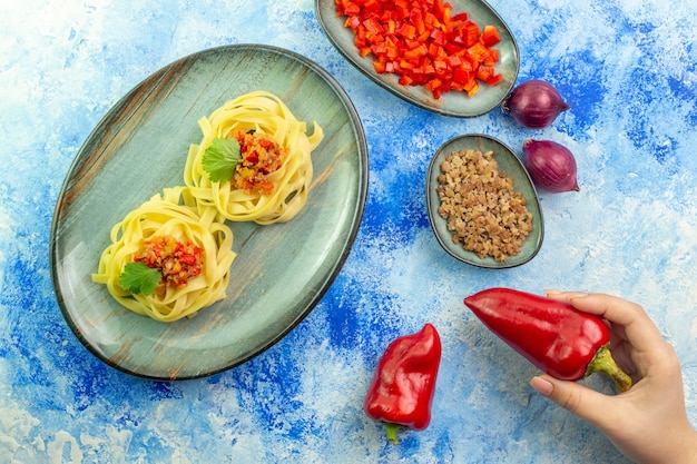 Top view of a blue plate with tasty pasta and necessary vegetables meat on blue table