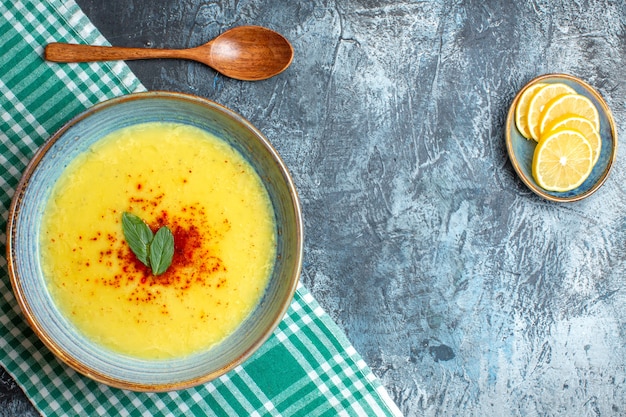 Free photo top view of a blue pot with tasty soup served with mint and pepper next to chopped lemon wooden spoon on blue background