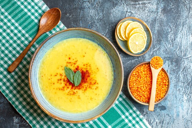 Top view a blue pot with tasty soup served with mint and pepper next to chopped lemon wooden spoon and yellow pea on blue background