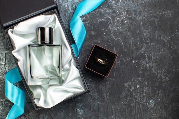 Top view of blue ribbon on man perfume in a gift box and engagement band on the right side on dark table