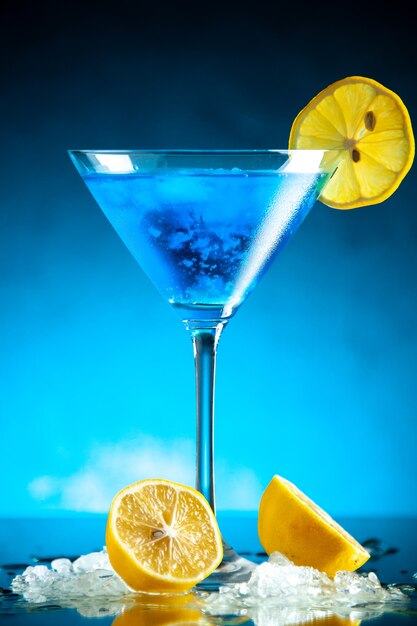 Top view of blue water in a glass goblet served with lemon slice and ice on the right side on dark background