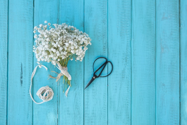 Top view of blue wooden surface with flowers and scissors