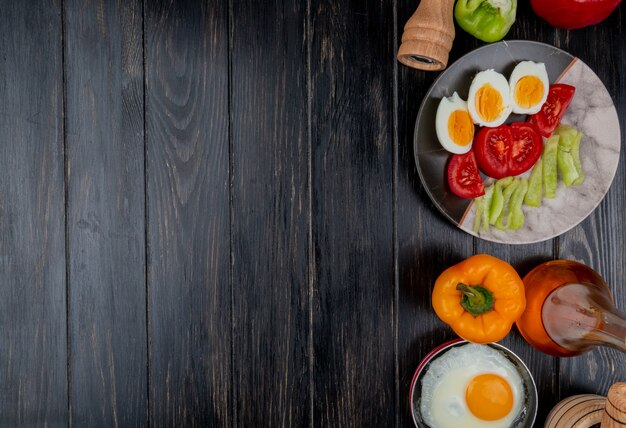 Top view of boiled eggs on a plate with slices of tomato with apple vinegar on a wooden background with copy space