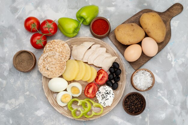 Вид сверху вареные яйца с маслинами грудки, свежие овощи и помидоры на серый, растительное питание еды завтрак