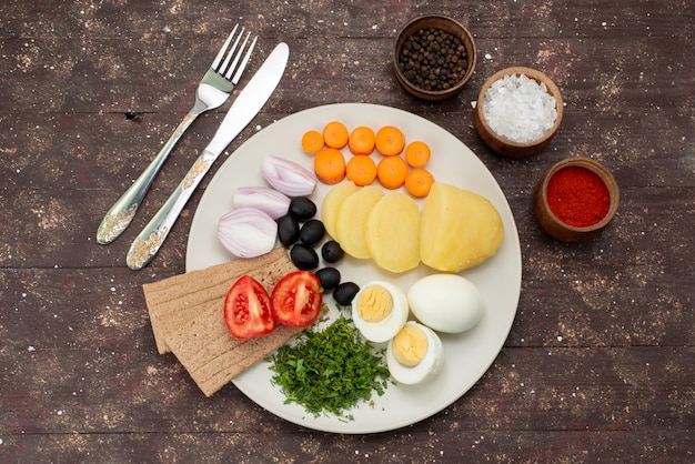 Top view boiled eggs with olives greens garlic seasonings and tomatoes on brown, vegetable food meal breakfast