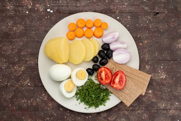 Top view boiled eggs with olives greens garlic and tomatoes inside plate on brown, vegetable food meal breakfast