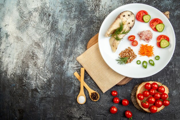 木製のまな板の上の裸のタオルと氷の表面のスパイスの上の白いプレートに野菜の緑を添えて煮魚そば粉の上面図