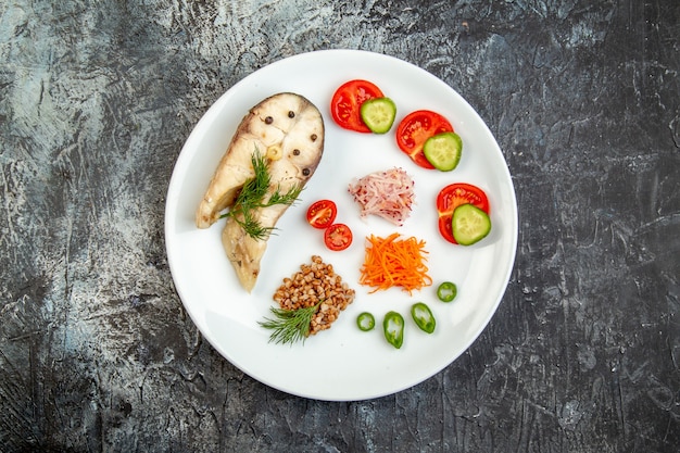 Top view of boiled fish buckwheat served with vegetables green on a white plate on ice surface